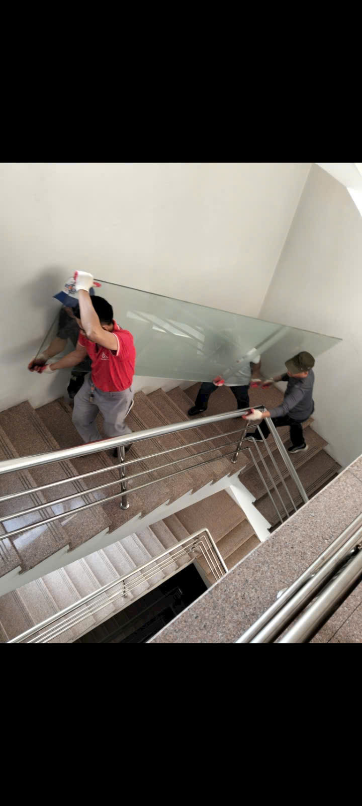 Đội ngũ vận chuyển tấm kính lớn qua cầu thang tại công trình